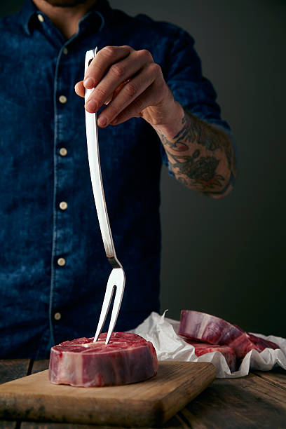 istock Tattoed butcher hand holds meat fork in fresh steak 500044798