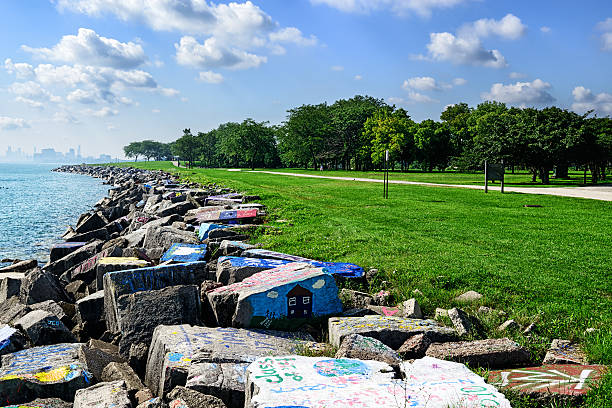 Lake Michigan Shireline in Evanston with distant Chicago Evanston, IL, USA - August 31, 2014: Riprap with graffiti , Lake Michigan shoreline in Evanston, Illinois.  Concrete blocks protecting the lakeshore. Chicago skyline in the distance. Distant people jogging in park. lake michigan photos stock pictures, royalty-free photos & images