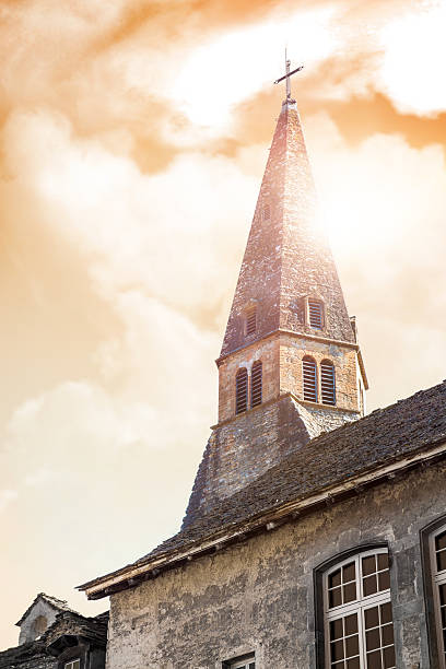 Vertical composition photography in HDR technic of steeple from Augustinian Convent building of medieval town of Cremieu in Isere, Rhone-Alpes region in France (Europe). The convent was founded in 1317 by the Dauphins de la Tour and has sustained numerous alterations after the Revolution. The cloister dates from the reconstruction work undertaken by the monks in about 1640, after the accidental collapse of part of the buildings. This picture was shot with a bright orange sky and sunset at twilight time of the day. The church is the former chapel of the Augustinian convent. In 1791, during the French Revolution, when all the convent buildings have been bought back, it became the parish church. It was built since the 14th century and is leaning back against the ramparts. Its particularity is that it’s facing south-north. During the 15th century, a second period of construction towards the north started. It was changed many times up to the 19th century, especially the roof that was initially oak-panelled and that has been replaced by Neo-Gothic vaults.