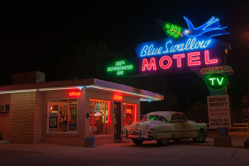 Tucumcari, New Mexico, USA - September 14, 2015: Blue Swallow Motel famous classic neon signs illuminated at night with white Pontiac parked in entrance a landmark Route 66 motel dating from 1939 and today a popular place to stay for Route 66 travelers.