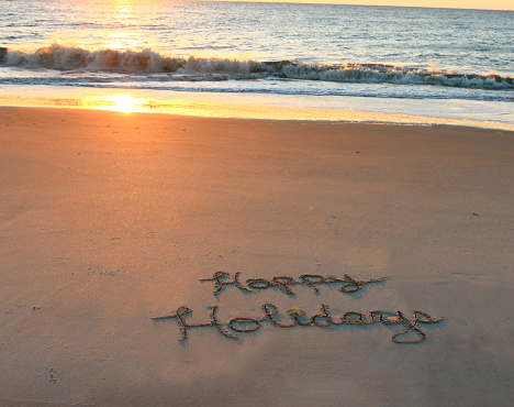 Happy Holidays written in sand.
