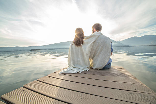 istock Young couple relaxes on lake pier, wrapped in blanket 500091298