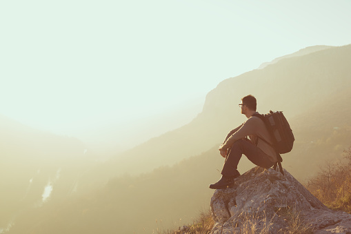 Male hiker sitting on a rock perched above the valley, admiring the spectacular view and enjoying the peace and quiet of a nature.