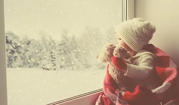 Photo of child little girl with  teddy bear at window winter
