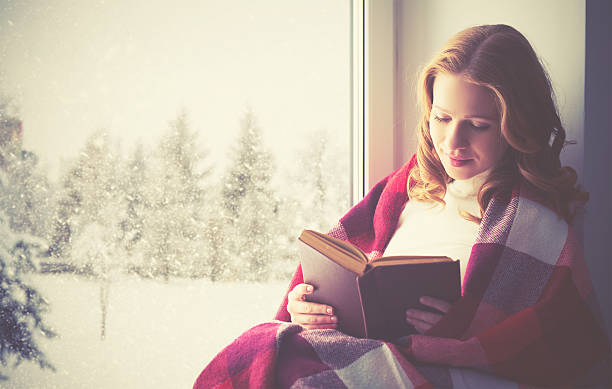 istock happy girl reading book by the window in winter 500093478
