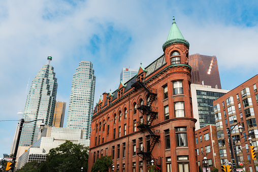 Toronto, Canada - September 5, 2015: Low-angle view of the Gooderham Building (the Flatiron Building) in downtown Toronto, a red-brick historic landmark of the city completed in 1892, with some modern buildings and skyscrapers in the background.