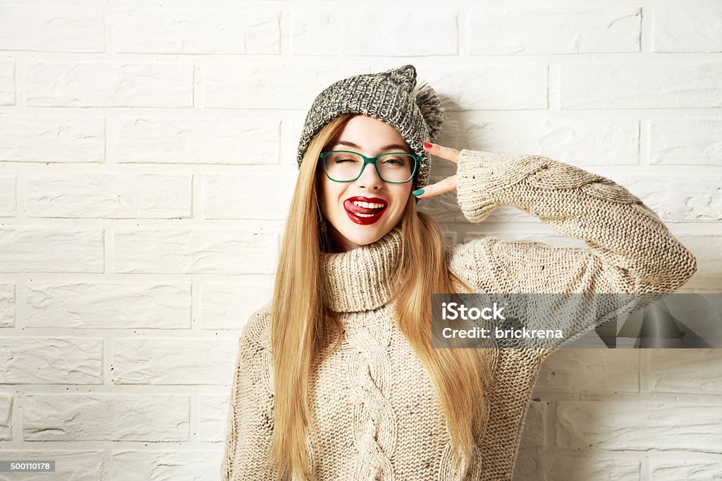 Funny Hipster Girl in Winter Clothes Going Crazy Funny Hipster Girl in Knitted Sweater and Beanie Hat Going Crazy at White Brick Wall Background. Trendy Casual Fashion Outfit in Winter. Toned Photo with Copy Space. Women Stock Photo
