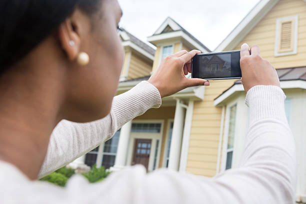 young woman taking photo of new home with smart phone - huis fotos stockfoto's en -beelden
