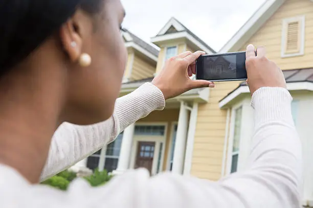 Young woman taking photo of new home with smart phone 