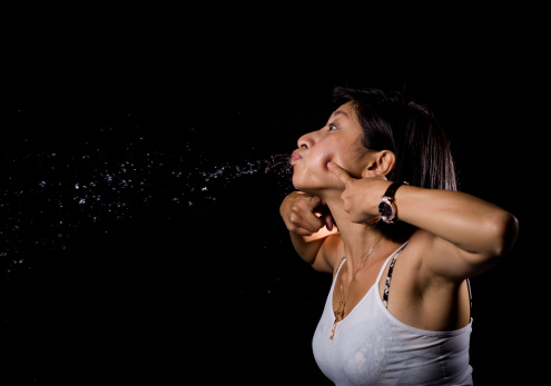A young Asian girl spitting against a black background