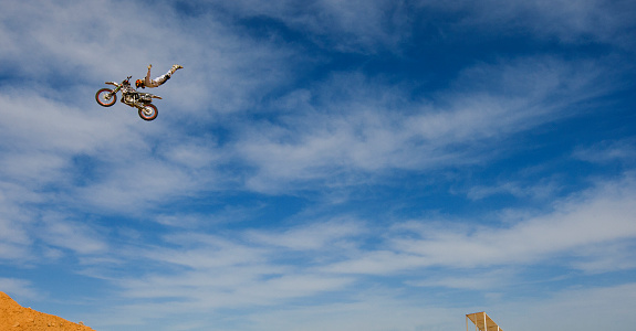 A male FMX or freestyle motocross rider does a Rock Solid trick off a big jump.