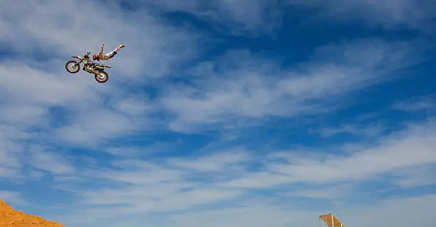 A male FMX or freestyle motocross rider does a Rock Solid trick off a big jump.