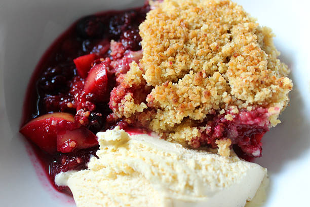 Image of apple and summer fruit crumble with ice cream Photo showing a tasty homemade apple and summer fruit crumble, served in a white dish with vanilla ice cream.  The fruit in the crumble include chopped apple, raspberries, blackberries, blueberries, cherries, redcurrants and blackcurrants. compote stock pictures, royalty-free photos & images