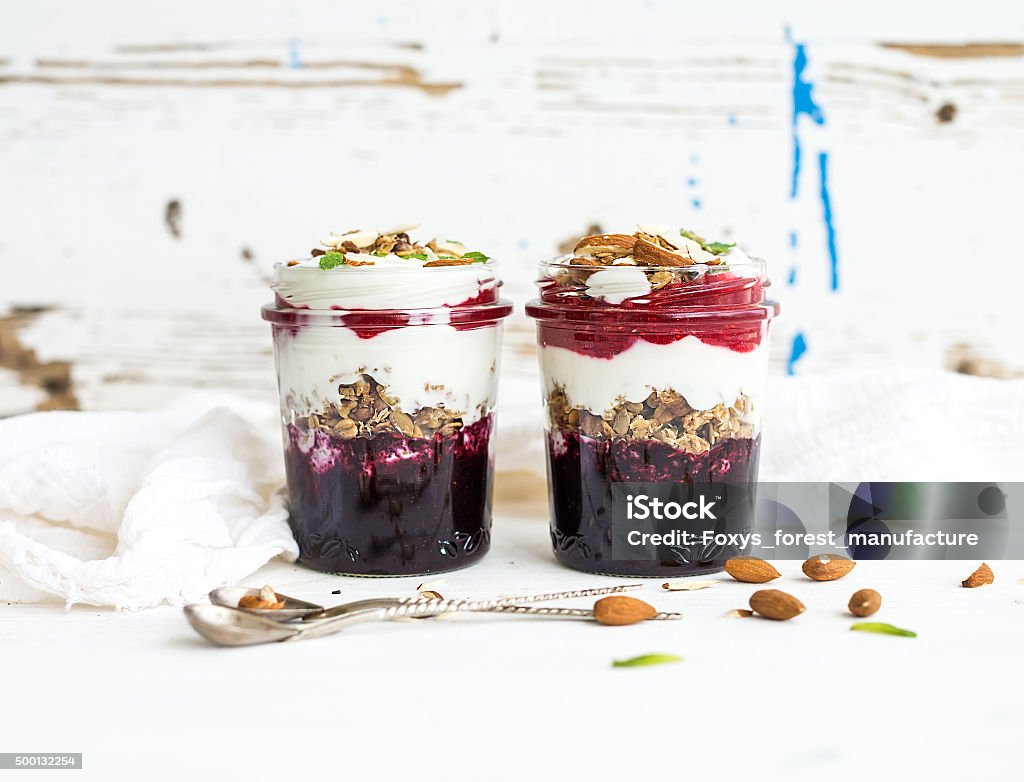 Yogurt oat granola with berries, honey and nuts in glass Yogurt oat granola with berries, honey and nuts in glass jars, rustic white backdrop Yogurt Stock Photo