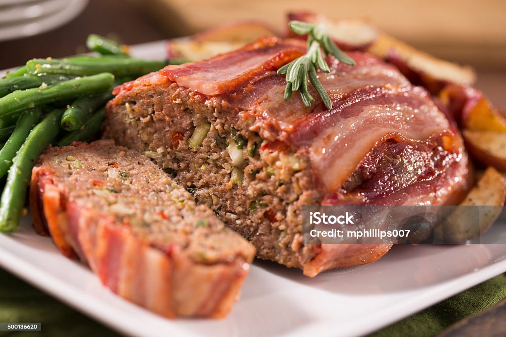 Bacon Wrapped Meatloaf A bacon wrapped meatloaf with green beans and roasted red potatoes.  The meatloaf is on a rustic farm table with a rustic cutting block in the background.  Please see my portfolio for other food and drink images.  Bacon Stock Photo