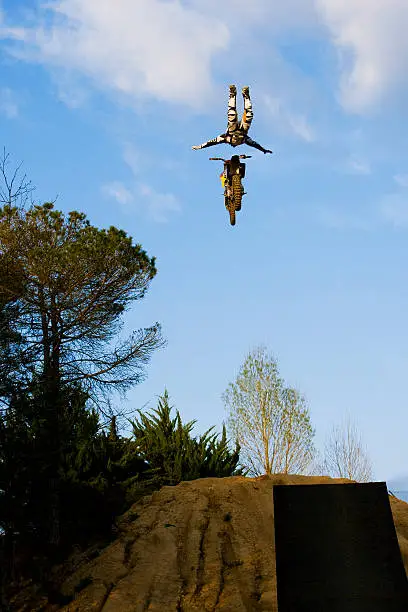 A male FMX freestyle motocross rider does a Rock Solid trick off a big jump.