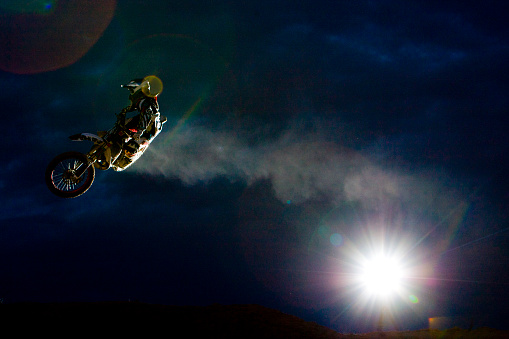 A male motocross rider hits a jump at night.