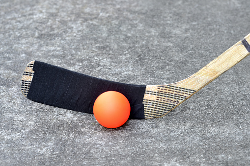 Close up of a well used hockey stick with hockey tape and ball on pavement.  