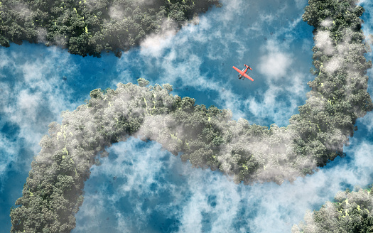 Aerial of red airplane flying over rainforest with river and clouds.
