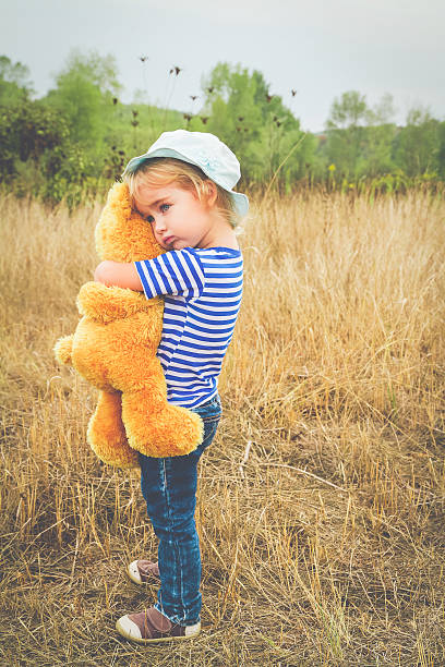 Cute little girl standing in the grass hugging a Teddy bear