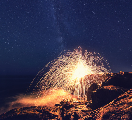 A ball of sparks showers down onto a rugged stretch of Nova Scotia coastline under clear Summer skies.  Long exposure.