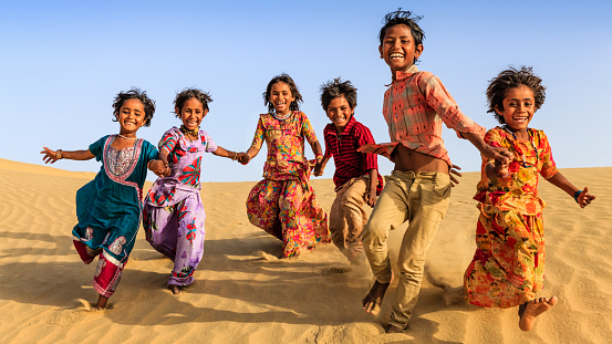 Group of happy Indian children running across sand dune - desert village, Thar Desert, Rajasthan, India.