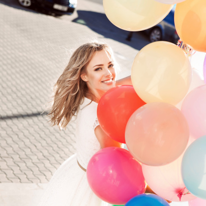 pretty smiling young woman in white summer dress with a bunch of multicolored balloons on sunny day in city