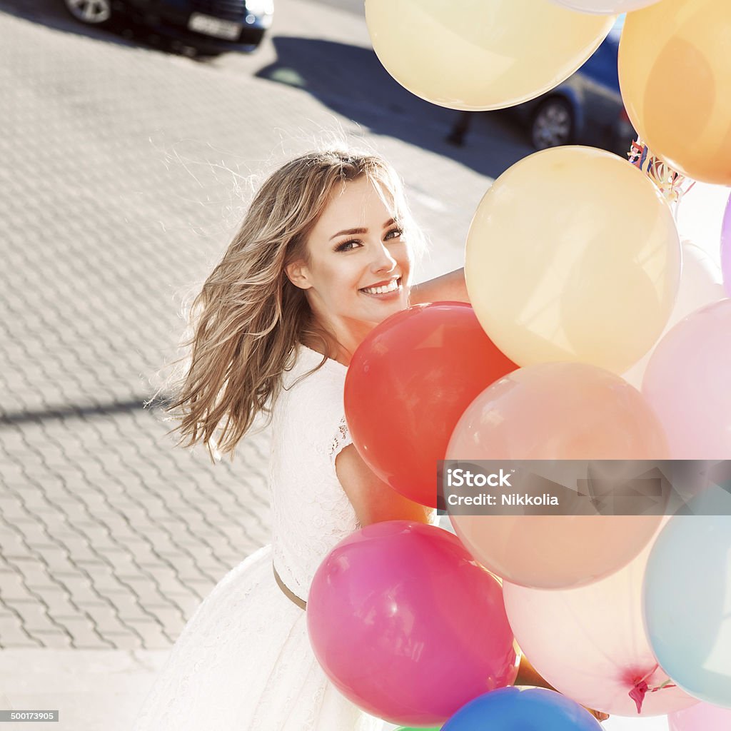 beautiful lady holding a bunch of balloons pretty smiling young woman in white summer dress with a bunch of multicolored balloons on sunny day in city Women Stock Photo