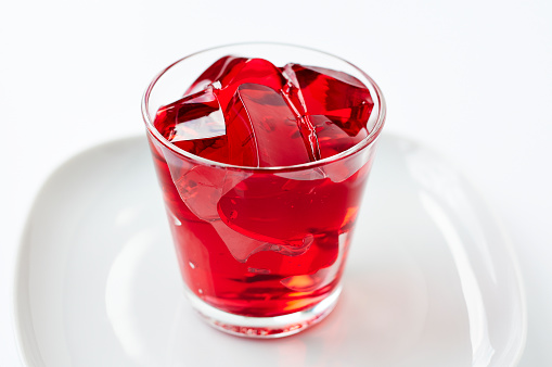 Red jelly cubes in a glass on a white background