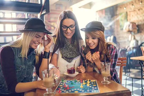 Young smiling women sitting in a cafe and having fun while playing board game.