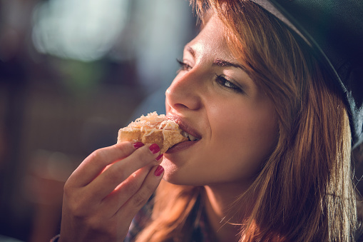 Close up of a smiling woman eating a small sandwich.