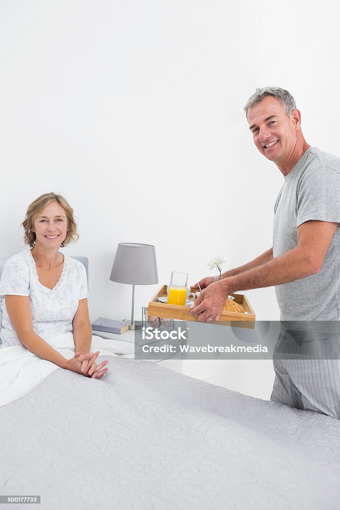 Sonriendo marido ofrecer el desayuno a su esposa en la cama - Foto de stock de 40-49 años libre de derechos