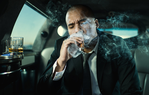 Mid adult African American businessman smoking a Cuban cigar while traveling in a limousine.
