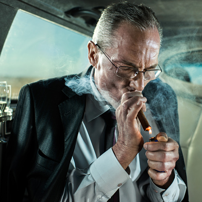 Mature businessman lighting up a cigar while traveling in a limousine.