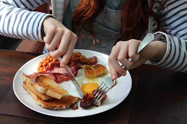 Girl eating full English fried breakfast, sausage, egg, bacon, baked-beans Photo showing a young girl eating a full English fried breakfast, consisting of sausage, bacon, fried egg, fried bread, baked beans and a hash brown. english breakfast stock pictures, royalty-free photos & images