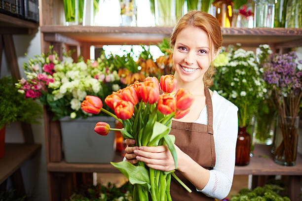 First tulips Portrait of young female florist with red tulips looking at camera florist stock pictures, royalty-free photos & images