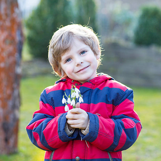 istock little kid boy in red jacket holding snowdrop flowers 500211666
