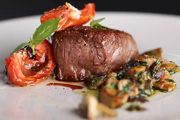 Photo of Roasted meat with tomatoes and mushrooms on a white plate