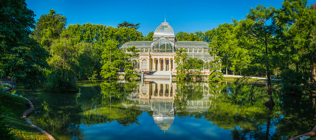 The glass and iron lattice of the 19th Century Palacio de Cristal reflecting in the tranquil waters of a lake set amongst the leafy green foliage of Buen Retiro Park in the heart of Madrid, Spain's vibrant capital city.  ProPhoto RGB profile for maximum color fidelity and gamut.