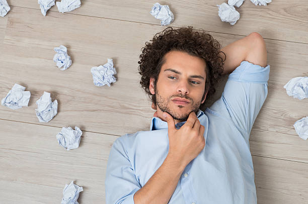 Man With Crumpled Papers Lying On Floor Contemplated Young Man Lying On Floor Surrounded With Crumpled Paper depression behavior businessman economic depression stock pictures, royalty-free photos & images