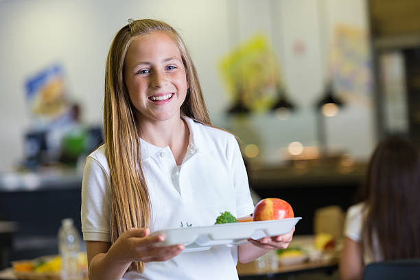 Preteen girl holding tray of cafeteria food in school lunchroom Preteen girl holding tray of cafeteria food in school lunchroom 12 13 years pre adolescent child female blond hair stock pictures, royalty-free photos & images