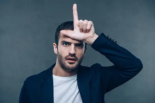Portrait of beautiful young man gesturing L sign while standing against grey background