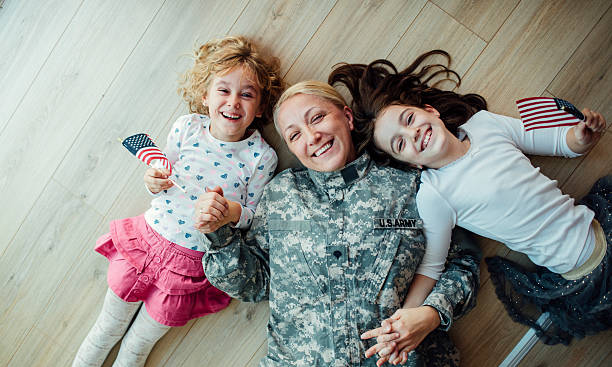 Army Mom Reunites With Her Little Girls. Military mom lying on floor with her two children, little girls. Looking at camera and smiling. Having some happy time together. Mother just return from some of army missions. Shot with Canon EOS 5Ds 50mp military lifestyle stock pictures, royalty-free photos & images