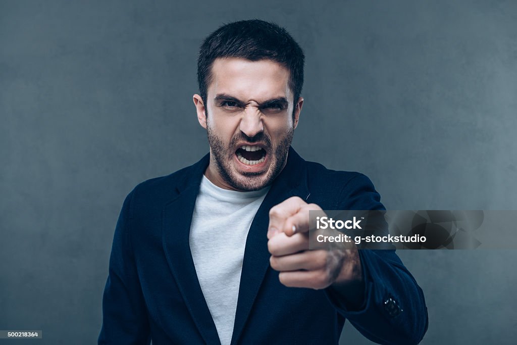 I know that was you! Furious young man looking at camera and pointing you while standing against grey background Anger Stock Photo