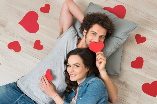 Loving Young Couple Holding Red Heart Together Lying On Floor