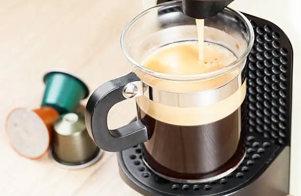 Single-serving coffee machine dispenses  espresso in a glass cup  with coffee capsules in background