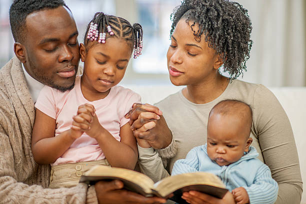A family of four are sitting on the couch together and are reading a Bible story.