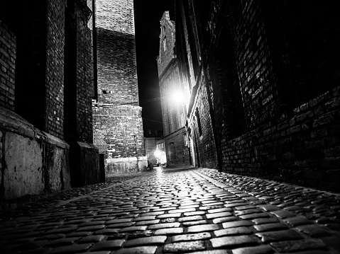 Illuminated cobbled street with light reflections on cobblestones in old historical city by night. Black and white image.