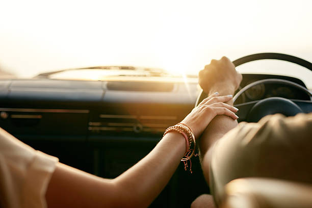 Young couple in their car holding hands Rear view of a young couple holding hands while sitting in their car together. Man and woman on a road trip. time period stock pictures, royalty-free photos & images