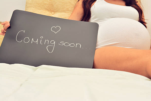 Coming soon pregnant woman with a sign that says coming announce stock pictures, royalty-free photos & images